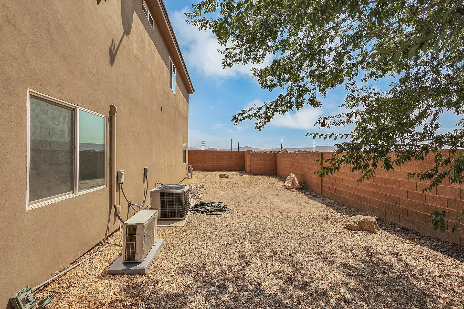 Stucco exterior with multiple windows, featuring a gravel yard, and a block wall perimeter