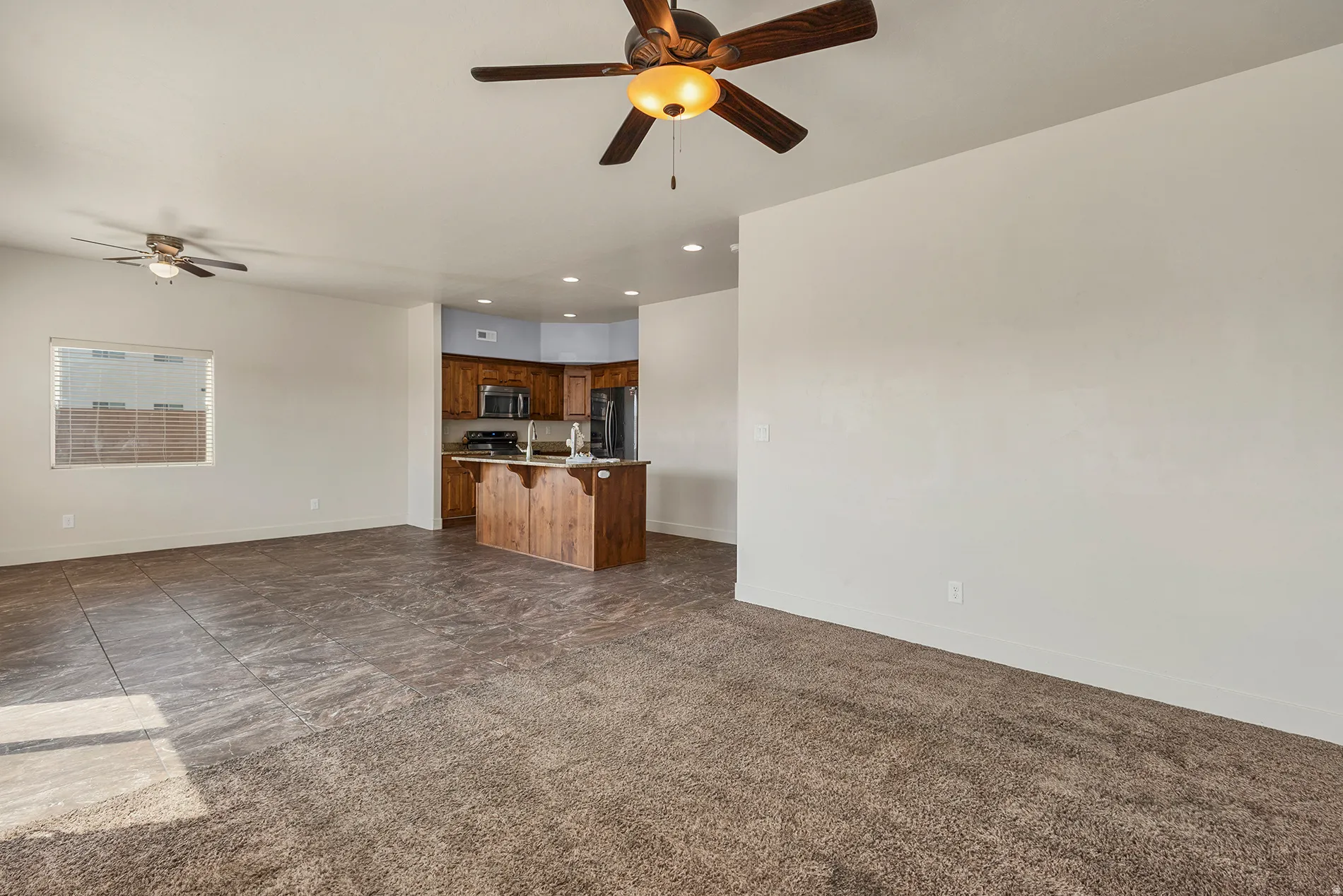 Open concept living space featuring a ceiling fan, a window with horizontal blinds, and a combination of carpet and tiled flooring