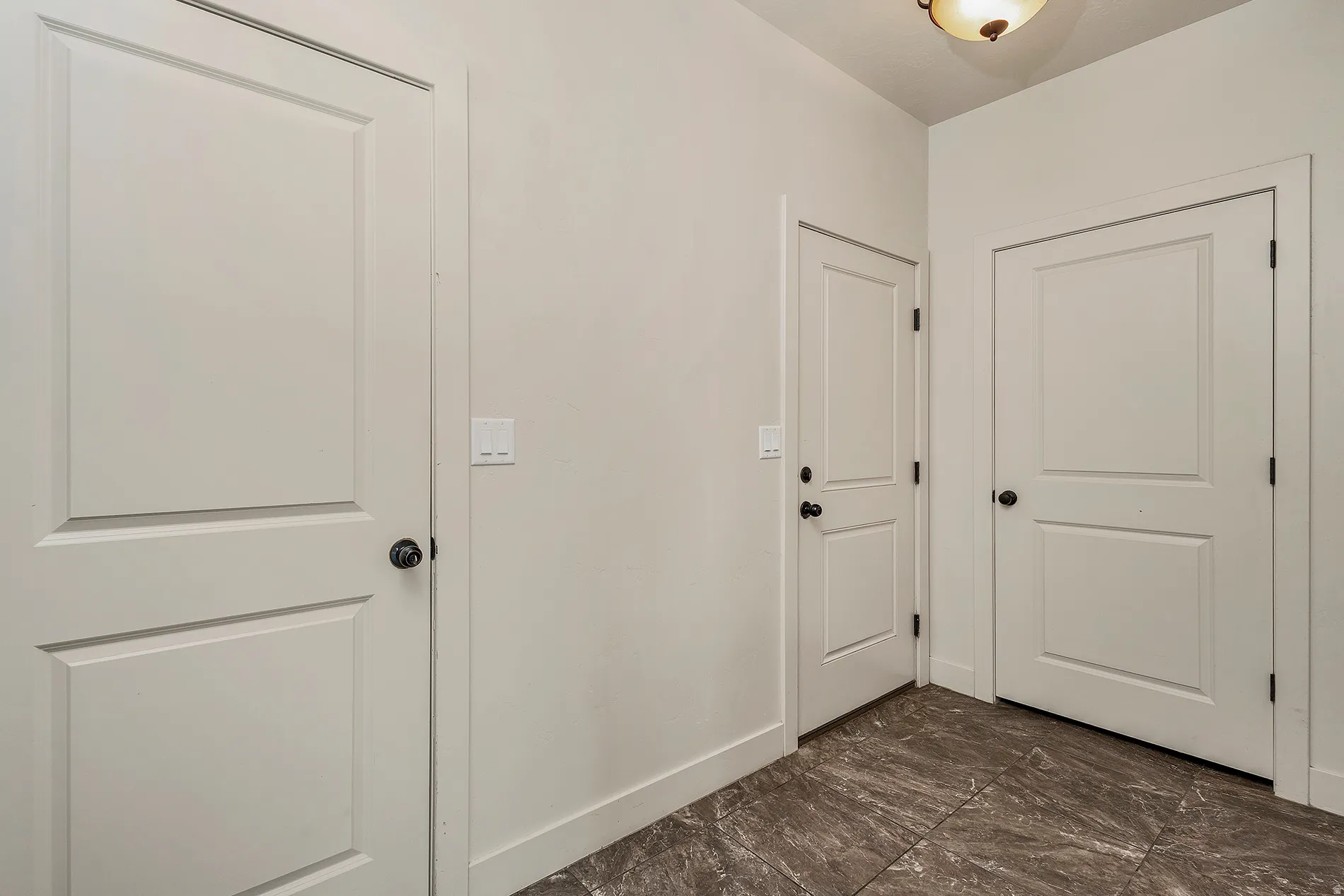 Three paneled doors with matte black hardware, light neutral wall paint, and dark stone-finish tile flooring