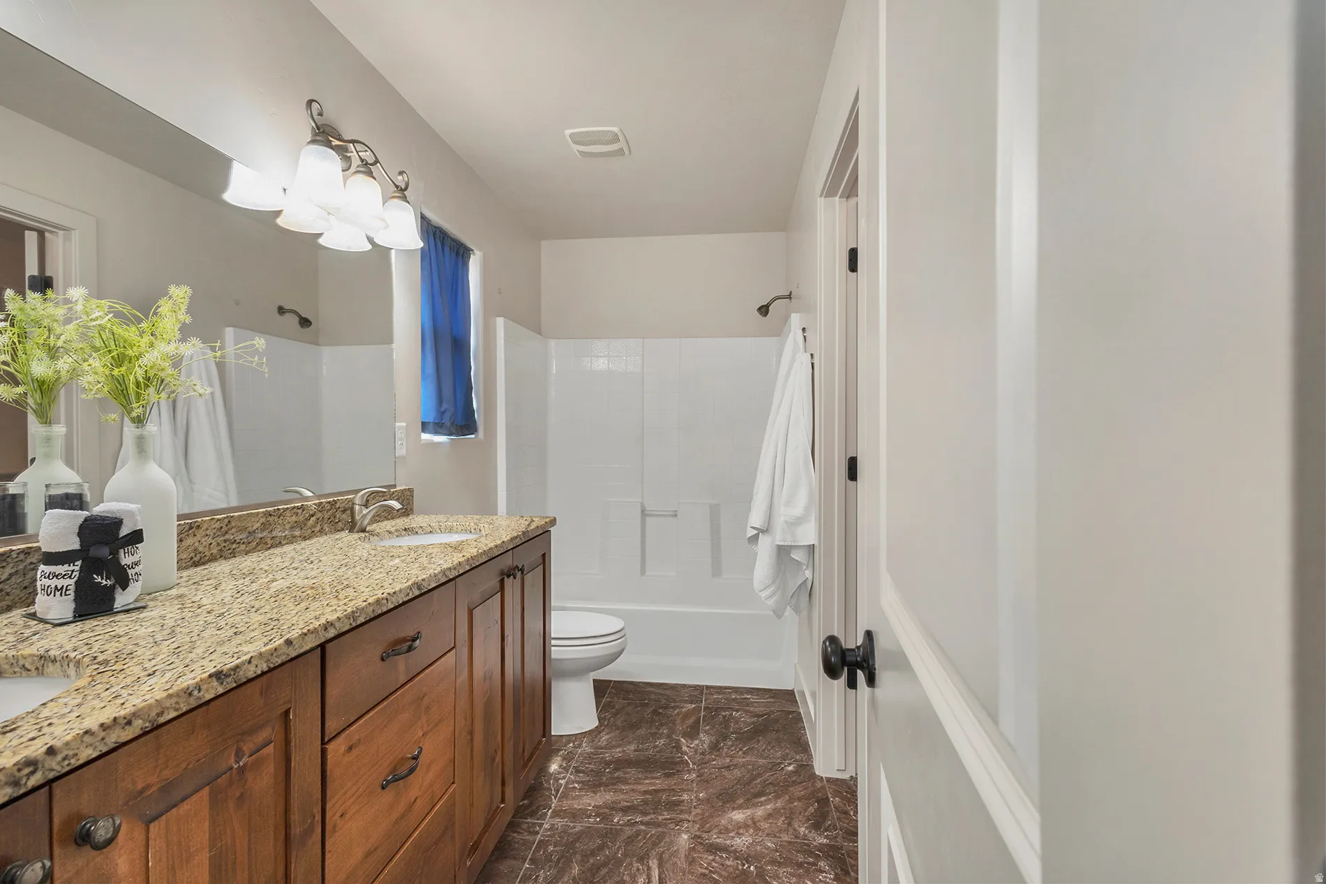Dual sink vanity with granite-style countertop, wood-finish cabinetry, and tiled flooring