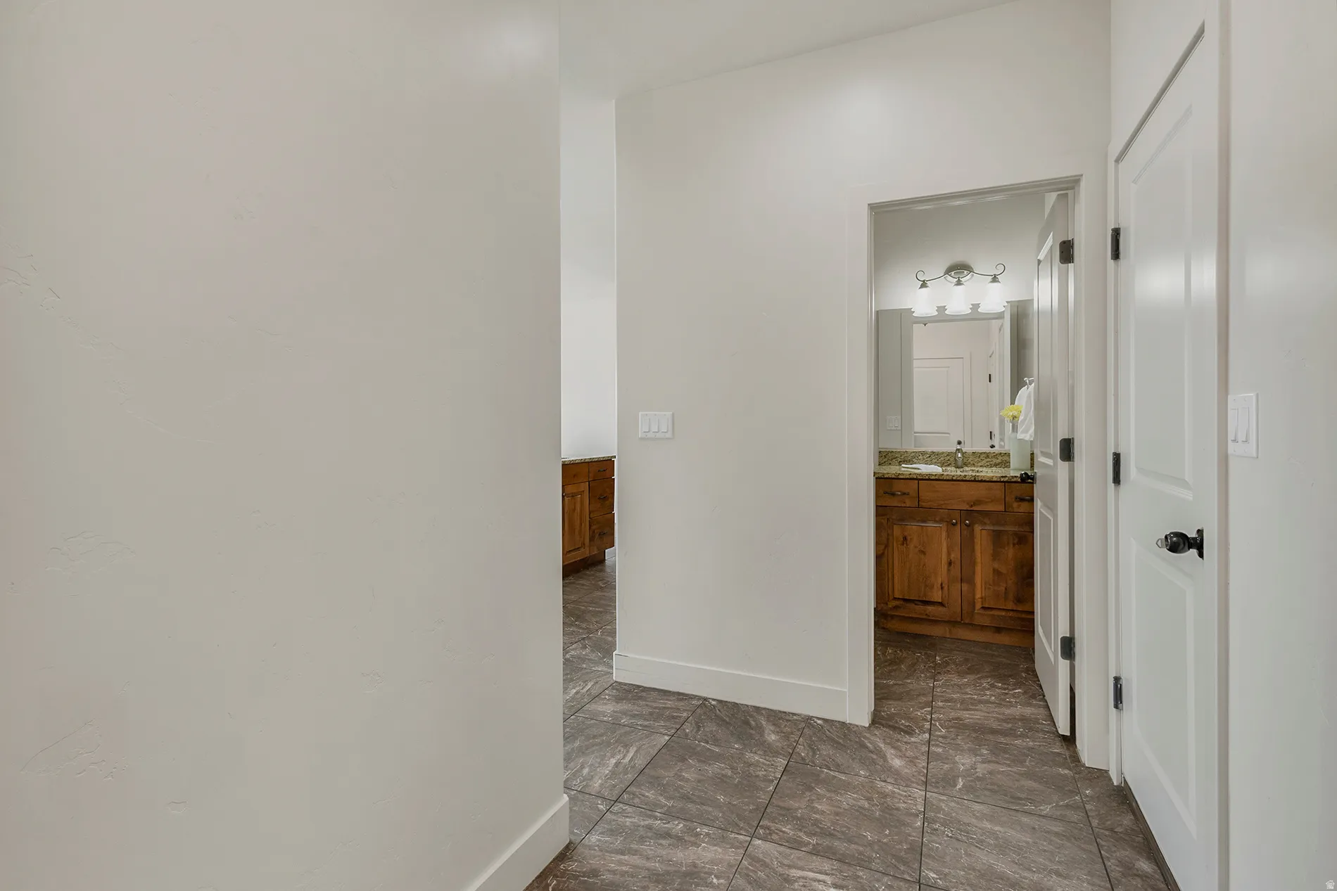 Tiled flooring extending into a full bathroom, featuring a wood-finish vanity with a countertop, and a vanity light fixture