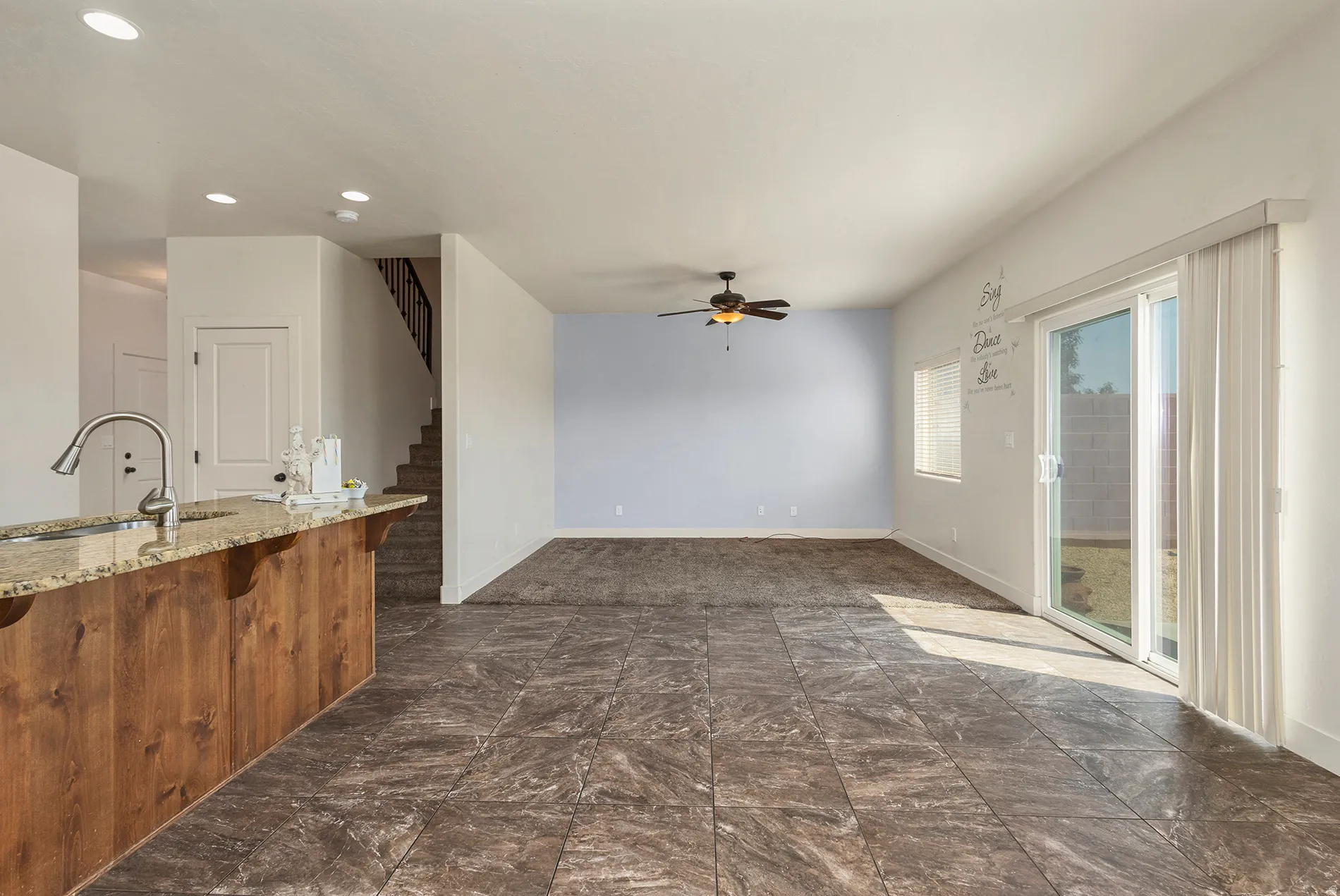 Granite-finish breakfast bar, stainless steel gooseneck faucet, recessed lighting, ceiling fan, and sliding glass door to outdoor space