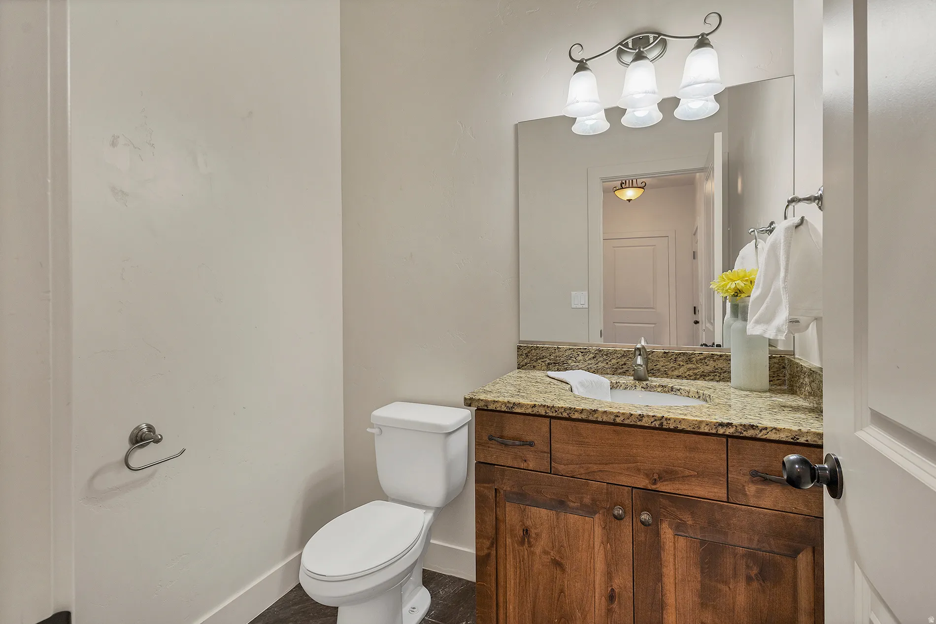Wood-finish vanity with a stone countertop, undermount sink, and wall-mounted mirror