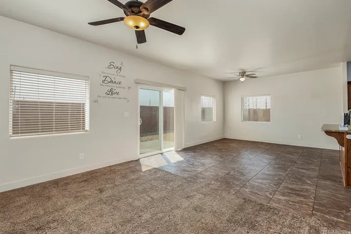 Spacious room featuring a sliding glass door, multiple windows, ceiling fans, and a combination of carpet and tile flooring