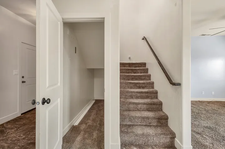 Bright hallway with generous closet storage, carpeted staircase with handrail, and wood-finish flooring in adjacent spaces