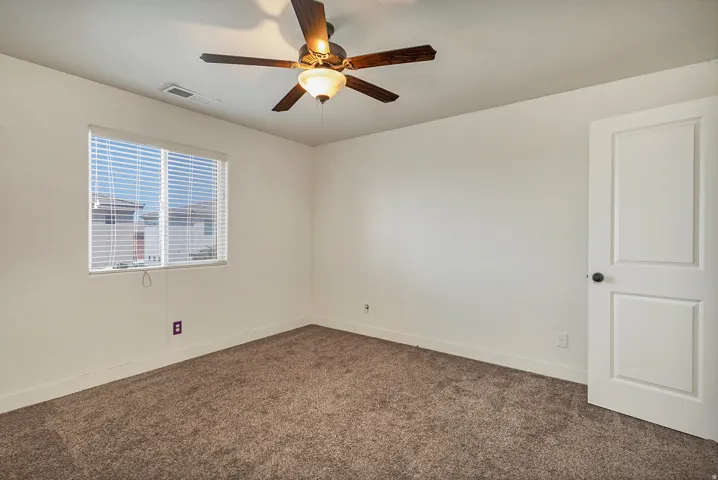 Carpeted flooring, white walls, window with blinds, ceiling fan with light fixture, and white paneled door with dark hardware