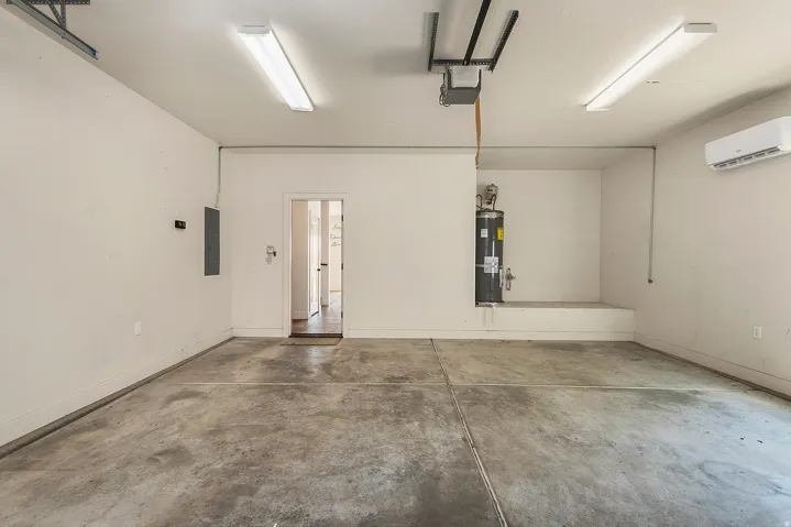 Concrete flooring with overhead fluorescent lighting, a built-in water heater platform, and a mounted ductless mini-split system