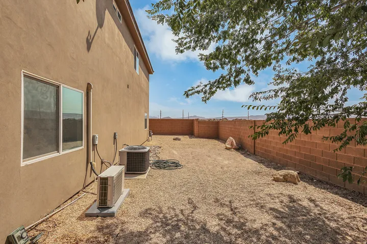 Stucco exterior with multiple windows, featuring a gravel yard, and a block wall perimeter