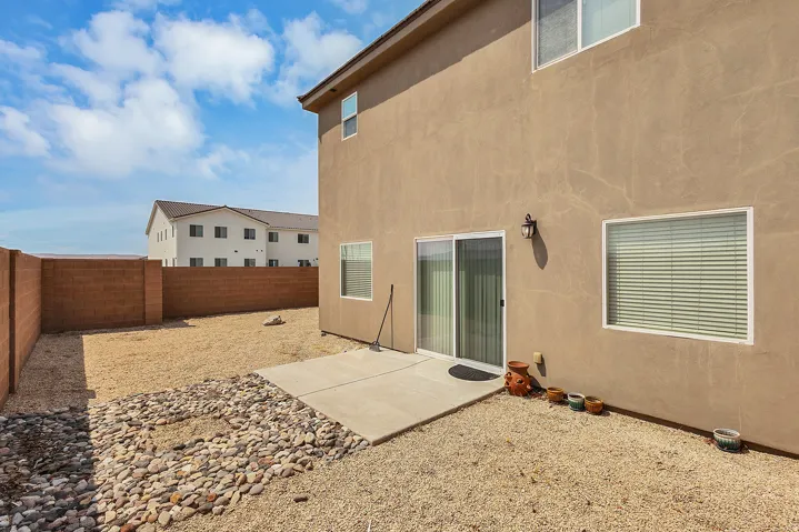 Exterior featuring stucco siding, sliding glass patio door, concrete patio, gravel landscaping, and a block wall perimeter