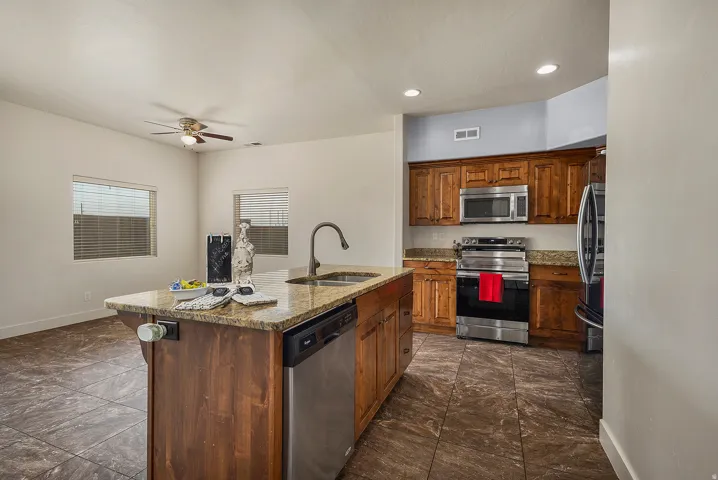 Kitchen featuring a central island with integrated sink, wood cabinetry, stone countertops, stainless steel appliances, and tiled flooring