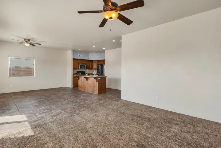 Open concept living space featuring a ceiling fan, a window with horizontal blinds, and a combination of carpet and tiled flooring