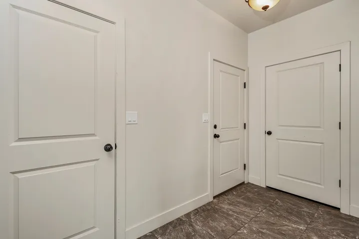 Three paneled doors with matte black hardware, light neutral wall paint, and dark stone-finish tile flooring