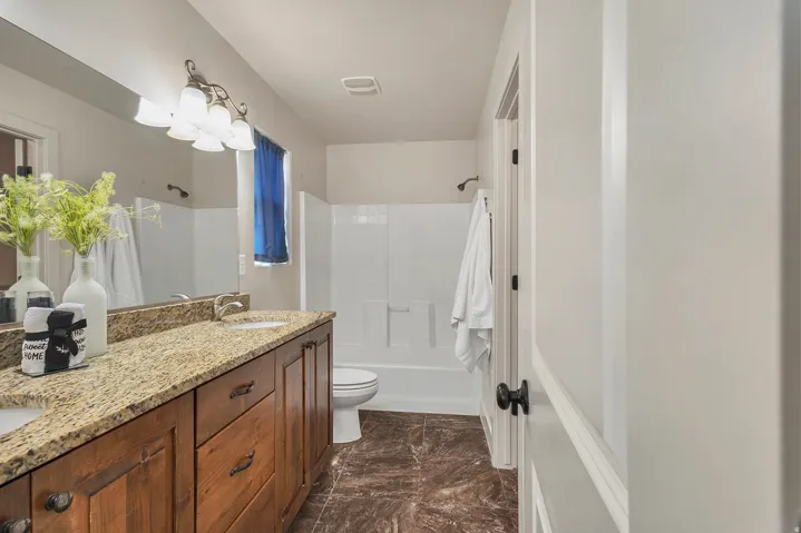 Dual sink vanity with granite-style countertop, wood-finish cabinetry, and tiled flooring