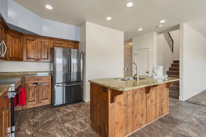 Kitchen featuring wood cabinetry, stainless steel refrigerator, granite countertops, and a central island with an integrated sink