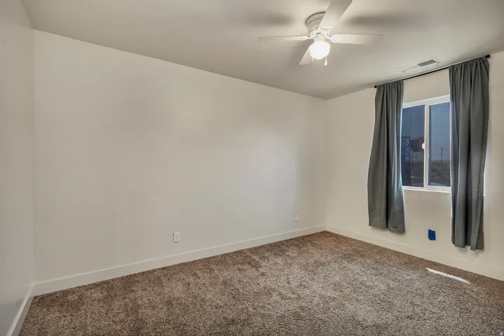 Carpeted room featuring a ceiling fan with integrated lighting and a double-pane window