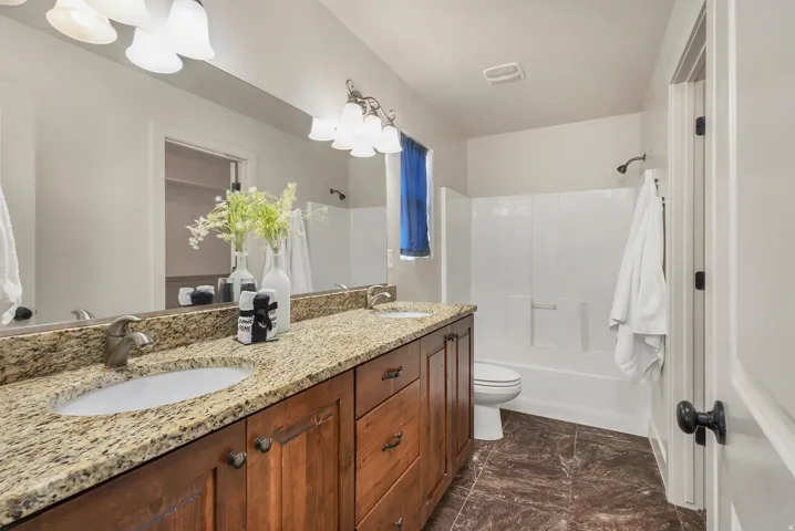 Double vanity with granite countertops, wood-finish cabinetry, dual undermount sinks, and an integrated tub-shower combination with tile surround