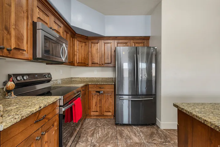 Kitchen featuring wood cabinetry, granite countertops, stainless steel appliances, and tile flooring