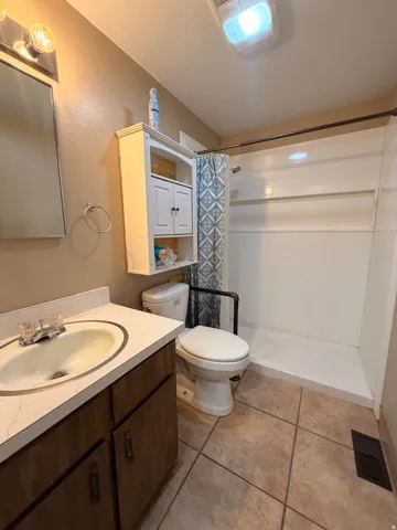 Bathroom featuring a vanity with an integrated sink, tile flooring, and a stand-up shower with grab bar