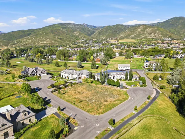Expansive undeveloped lot featuring a level terrain, surrounded by established residential properties and natural green spaces, with distant mountain ranges