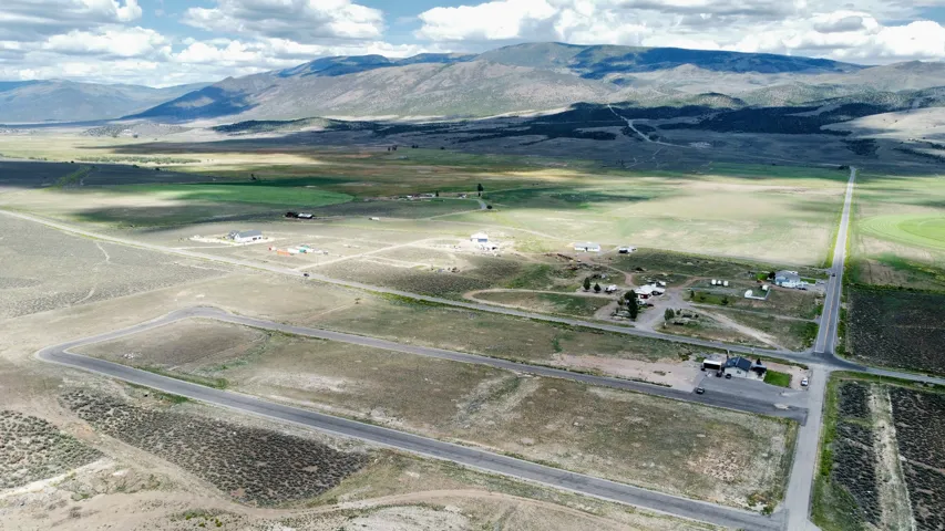 Expansive land parcels with distant mountain backdrop, featuring paved road access, scattered residential structures, and agricultural areas
