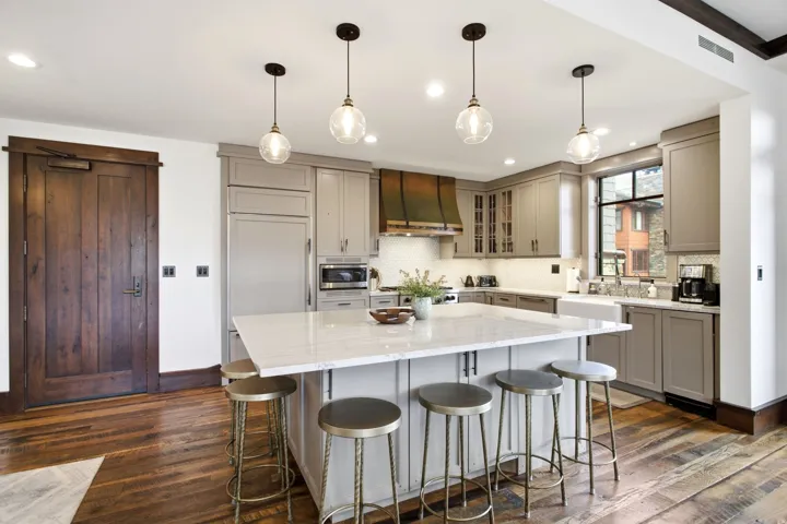Wood-finish flooring, central island with seating, white countertop, farmhouse sink, and a copper range hood
