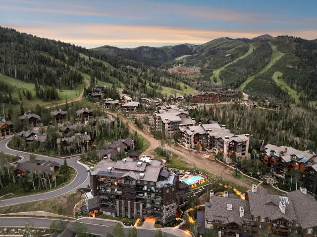 Mountainous terrain with extensive tree coverage, featuring multiple residential buildings and a distinct swimming pool area