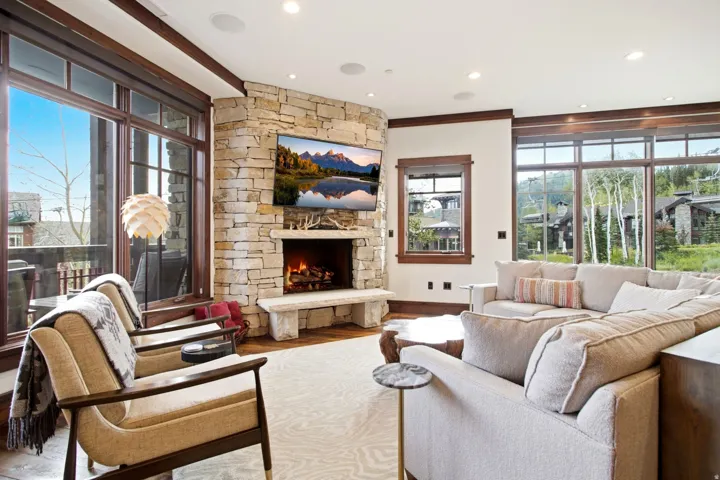 Corner stone fireplace with a substantial hearth, large picture windows, wood-framed windows, wood-finish flooring, and recessed ceiling lighting