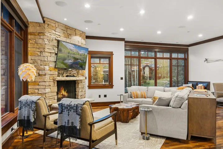 Stone-clad fireplace, rich wood-finish flooring, recessed lighting, and expansive multi-pane windows with dark wood trim