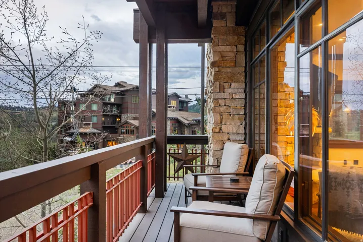 Balcony featuring durable wood-finish decking and railings, natural stone wall cladding, and expansive window panels