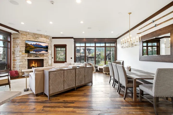 Stone-clad fireplace, wood-finish flooring, recessed lighting, expansive windows, and a multi-light chandelier