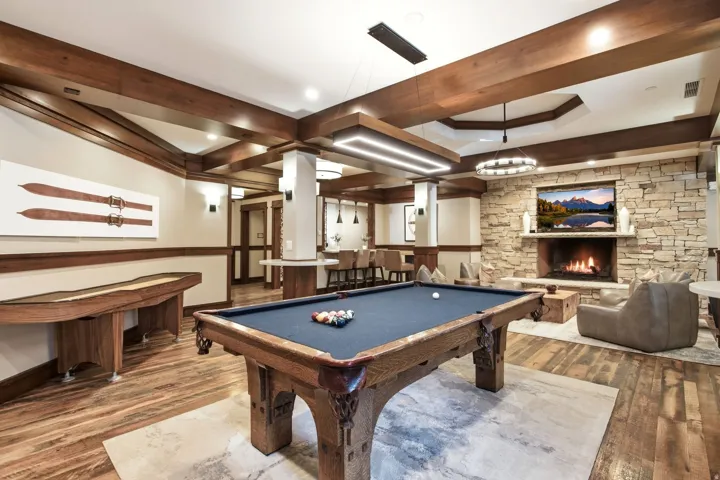 Wood-finish flooring, exposed wood beams, stone fireplace, recessed lighting, and a built-in wet bar