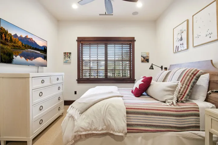 Recessed ceiling lighting, wood-finish window blinds, dark wood-finish window trim, light wood-finish headboard, built-in ceiling fan