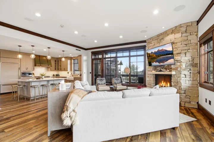 Open-concept living area with wood-finish flooring, a stone-clad fireplace, and a kitchen featuring a large island with seating