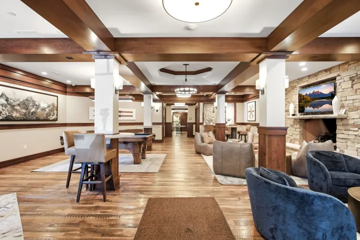 Hardwood flooring, exposed wood beams, wood wall paneling, stone fireplace, and recessed ceiling lighting