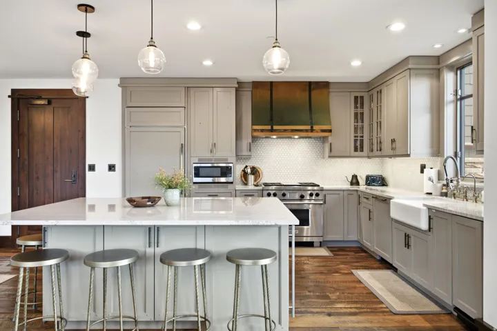Kitchen featuring a large island with a light-toned countertop, stainless steel appliances, custom range hood, farmhouse sink, and wood-finish flooring