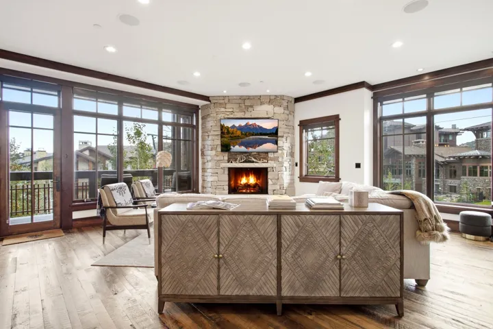Stone-clad corner fireplace, wood-finish flooring, recessed lighting, and expansive windows with dark wood trim