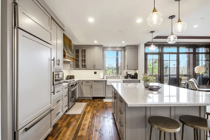 Gourmet kitchen featuring a built-in paneled refrigerator, wood-finish flooring, a farmhouse sink, a large island with seating, and expansive glass doors