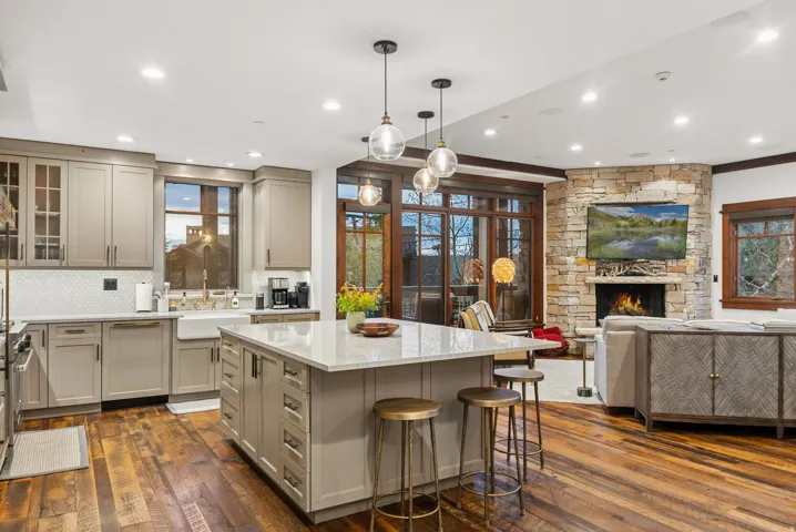 Kitchen and living area featuring wood-finish flooring, stone-clad fireplace, built-in cabinetry, center island with seating, and recessed lighting