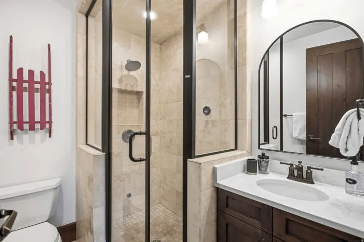 Enclosed glass shower with tiled walls and floor, vanity with stone countertop, and dark wood-finish cabinetry