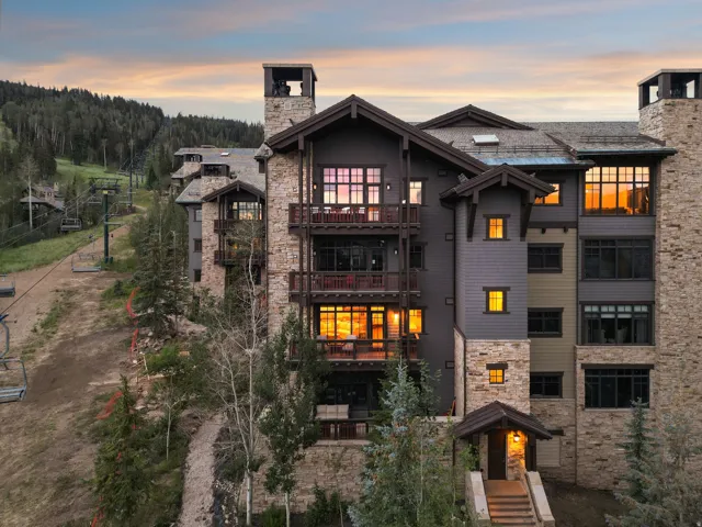 Multi-level building exterior featuring extensive stone cladding, multiple private balconies, and a covered entry with stone steps