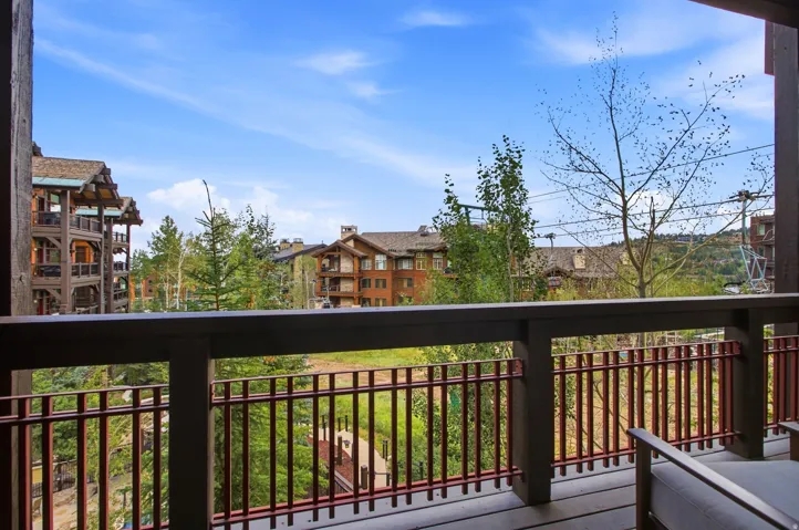 Expansive balcony featuring dark wood railings and a metal balustrade, overlooking a treed landscape with distant buildings