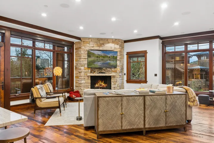 Corner stone fireplace with a built-in television, wood-finish flooring, recessed lighting, and large wood-framed windows