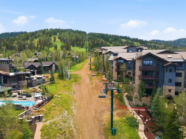 Stone and timber-clad multi-story buildings with balconies, featuring a ski lift and a resort-style pool with integrated seating