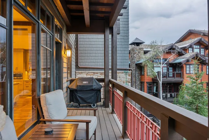 Expansive outdoor balcony featuring wood-finish decking, dark wood railing with red metal accents, and a built-in outdoor light fixture