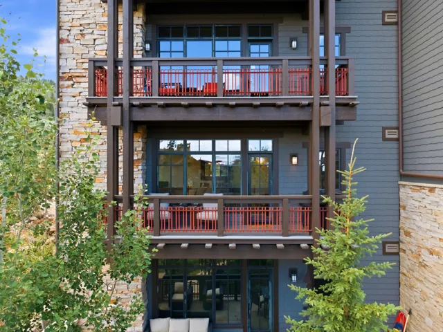 Stacked balconies with red metal railings and wood structural supports, stone veneer exterior, and horizontal siding