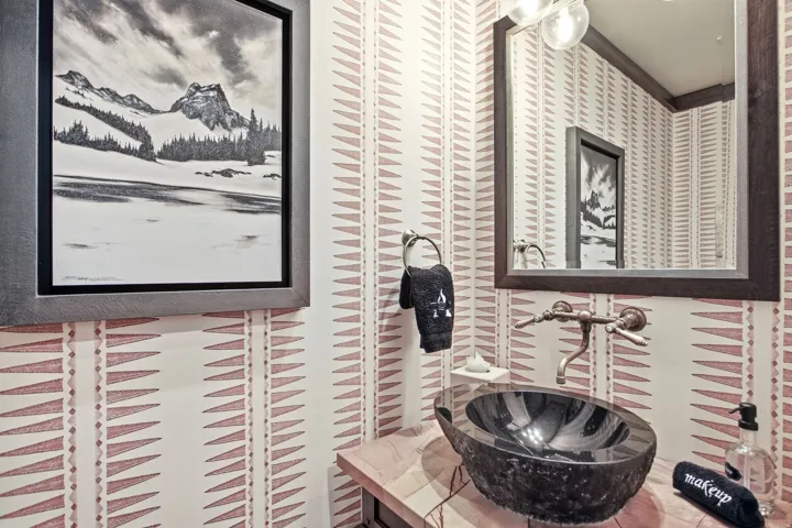 Patterned wallpaper accentuates a unique vessel sink, wall-mounted faucet, and wood-framed mirror