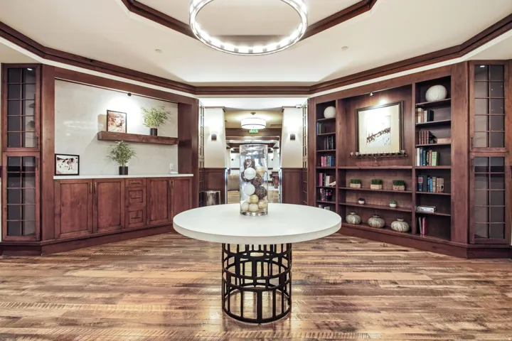 Wood-finish flooring, built-in shelving, rich wood paneling, circular chandelier, and a central round table
