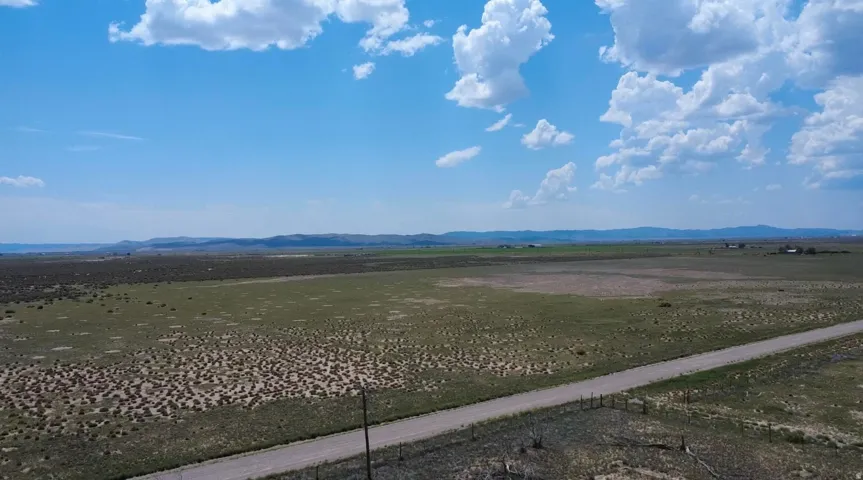 Expansive rural property featuring a gravel road, open fields, distant mountains, and a clear sky