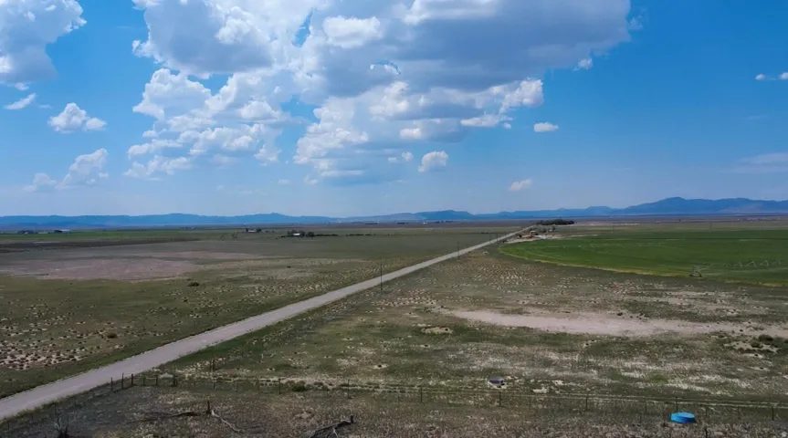 Expansive open land with a gravel road, distant mountain range, and scattered green fields