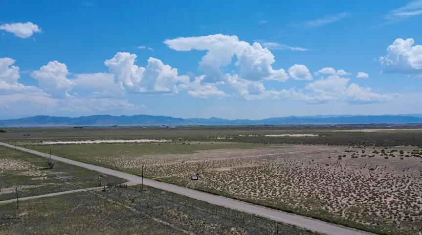 Expansive undeveloped land featuring a dirt road, sparse vegetation, and distant mountain ranges under a clear sky